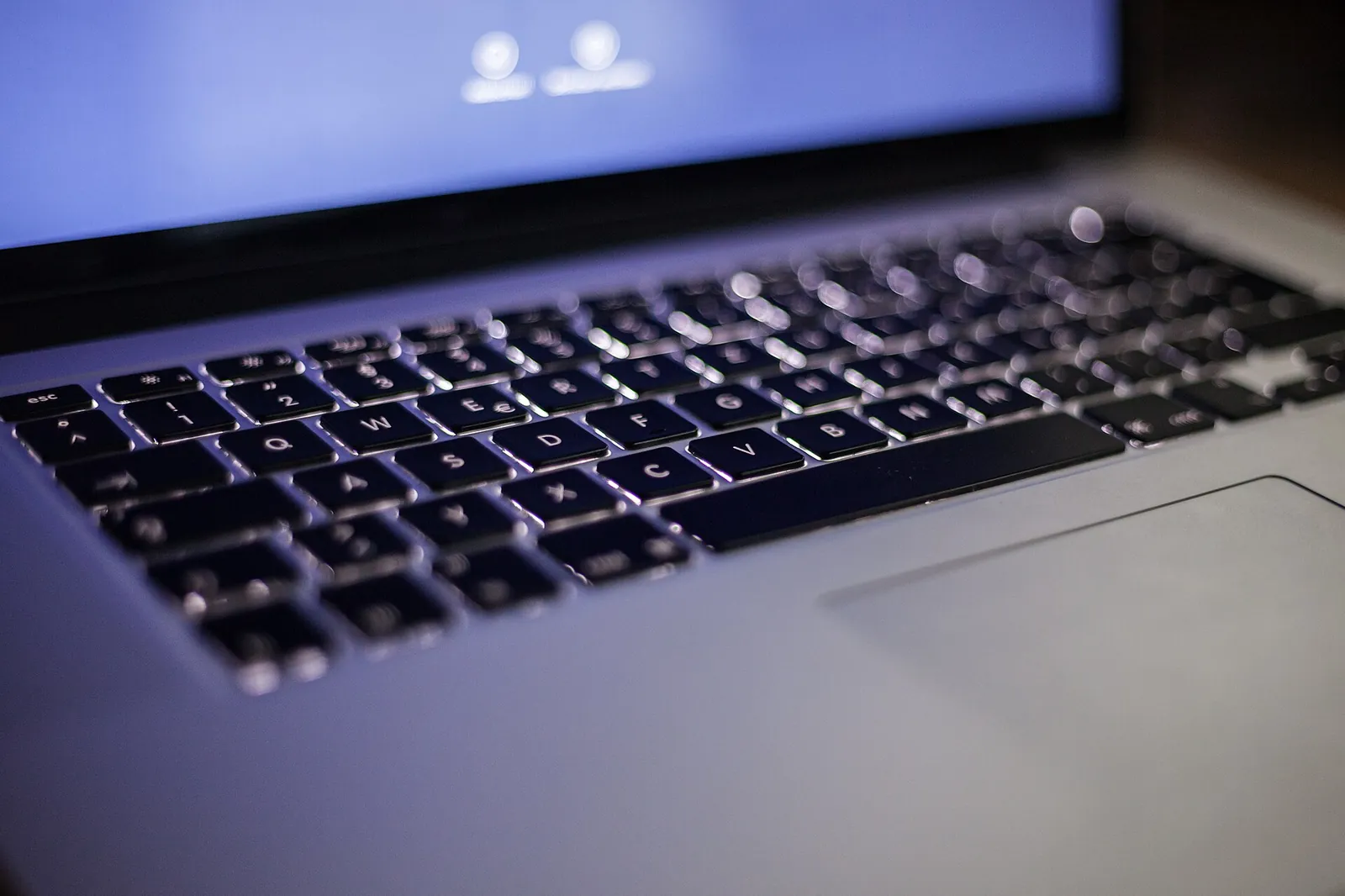 Podświetlona klawiatura laptopa i niebieskawy ekran w ciemnym pomieszczeniu